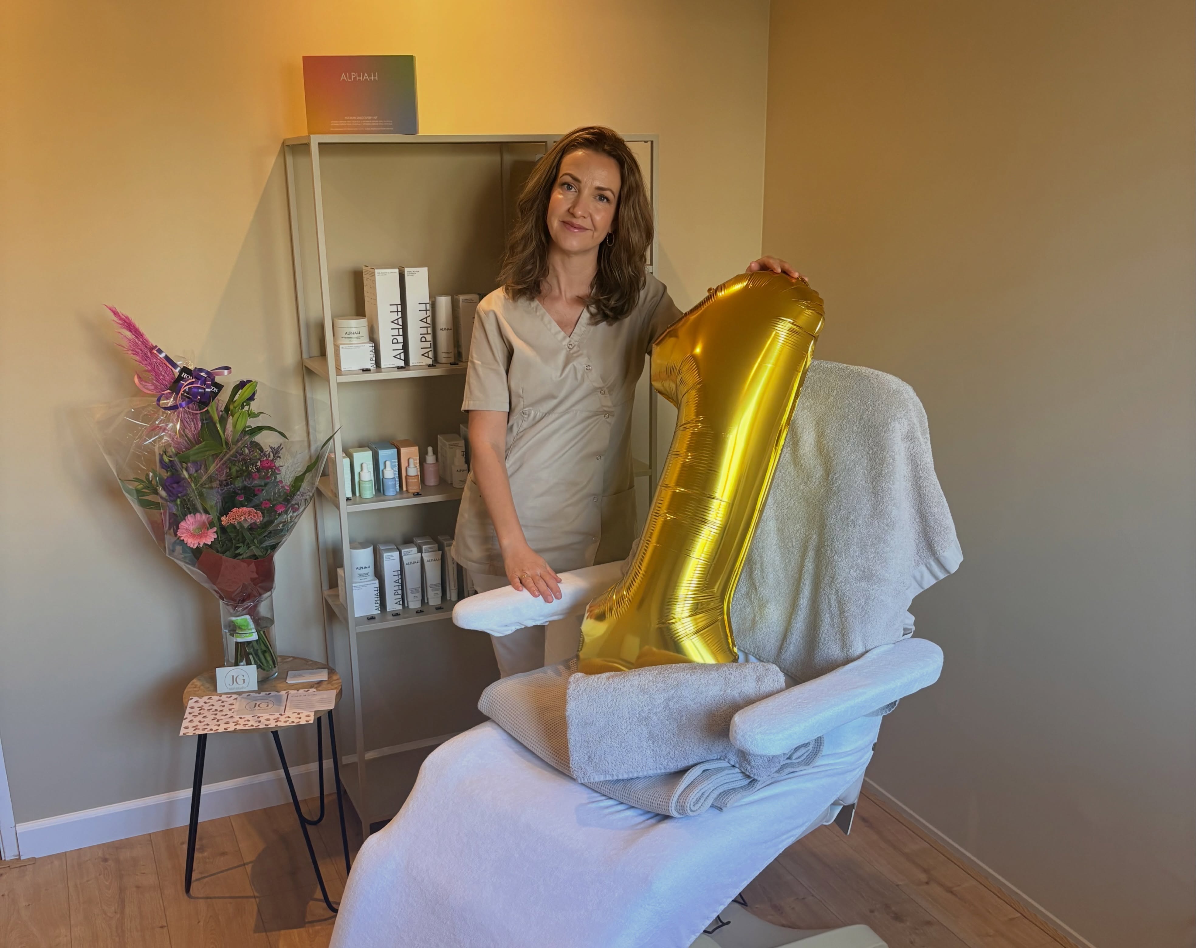 Joyce naast de behandelstoel met bloemen en een gouden ballon in de vorm van een 1