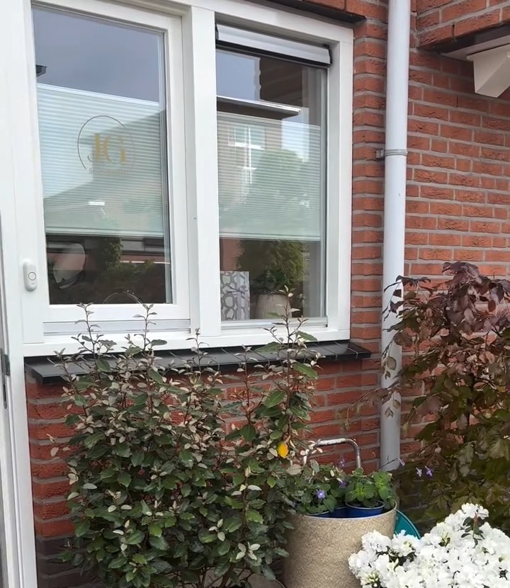 Het raam van de studio met het JG logo op het glas, met planten ervoor